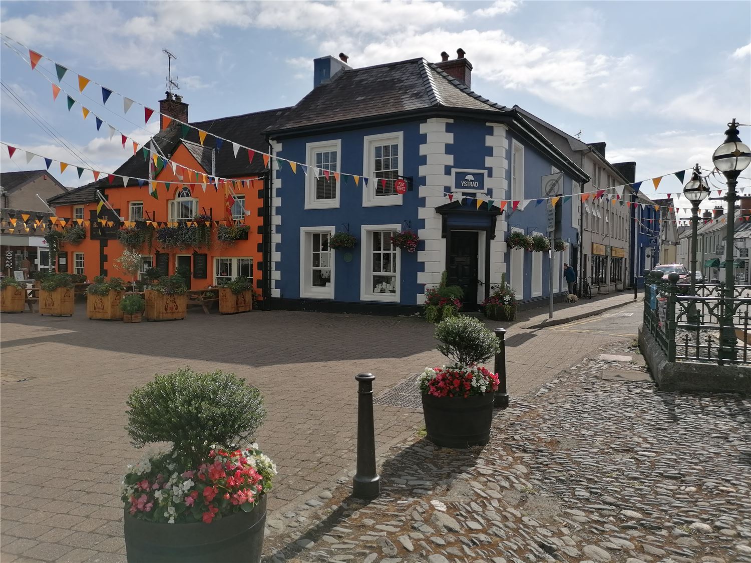 Picturesque Llandovery Market Square in Carmarthenshire, West Wales, featuring a traditional Welsh pub, colourful independent shopfronts and hanging flower baskets near the Brecon Beacons.